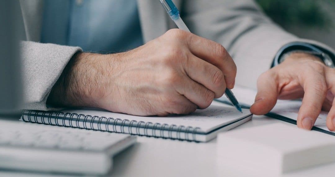 A man in a suit writing on a notebook