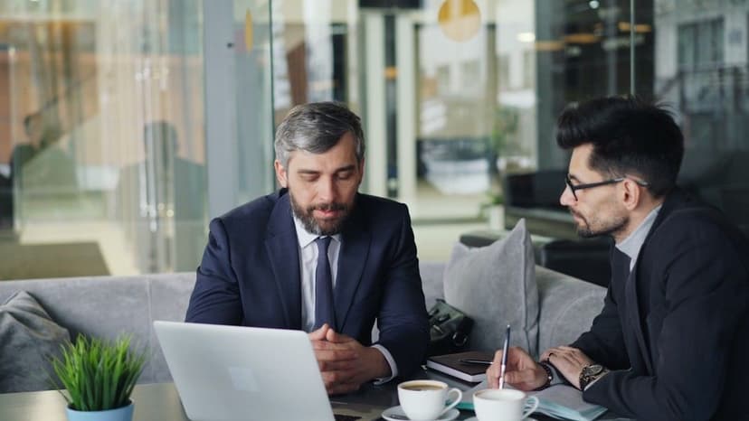 two men sitting at a table working on a laptop