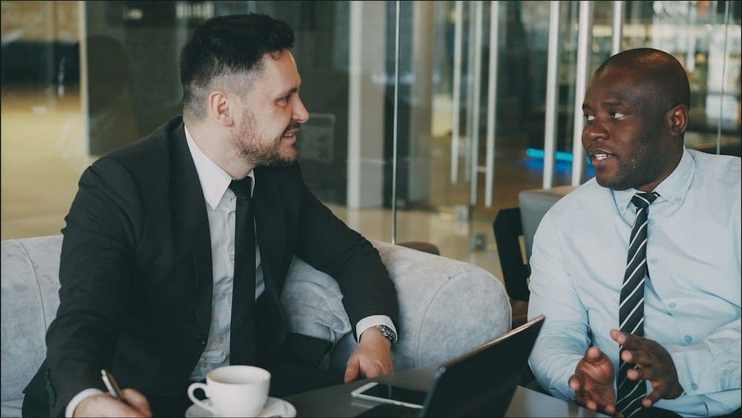 Two businessmen in suits talking at a table.