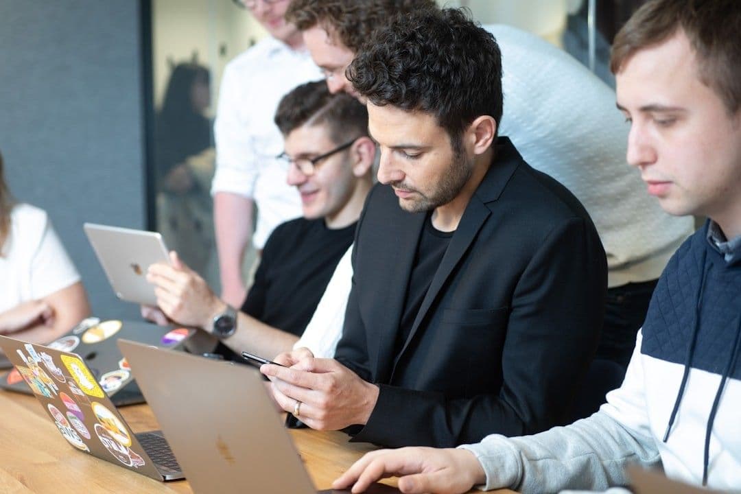 a group of people sitting at a table with laptops