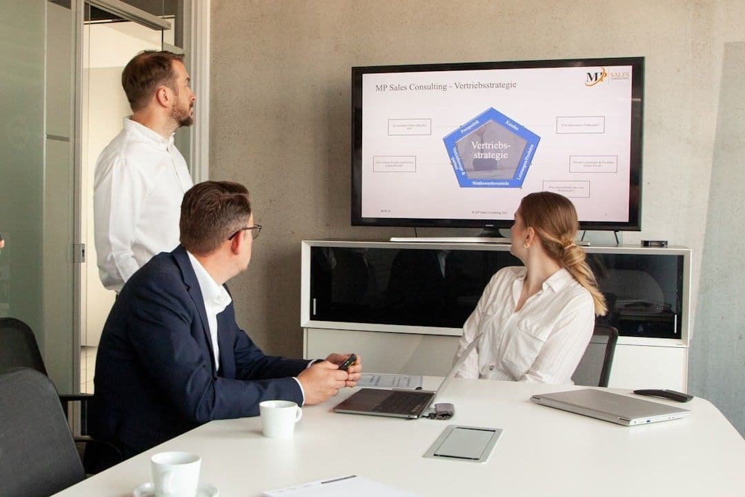 Three people in a meeting room looking at a presentation.
