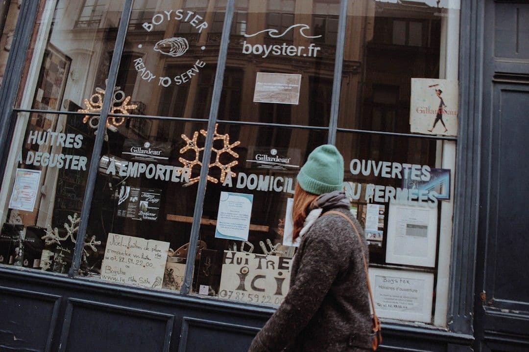 man in brown coat and green knit cap standing in front of store