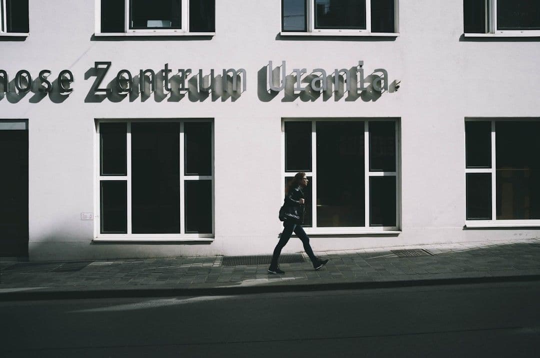 man in black jacket and pants walking on sidewalk in front of white and black building