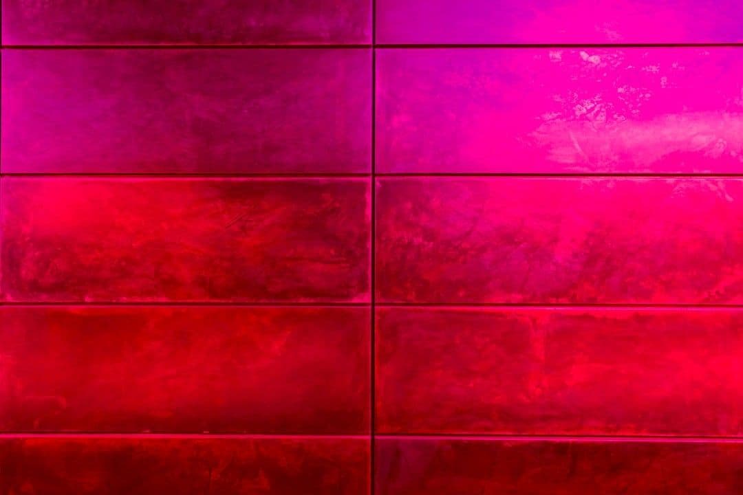 a red tiled wall with a red vase on top of it